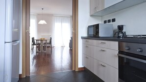 A modern kitchen with a microwave, coffee maker, and oven. There is a dining area with a table and chairs. - Italianway Comfort - Zanella 10 (Milan)