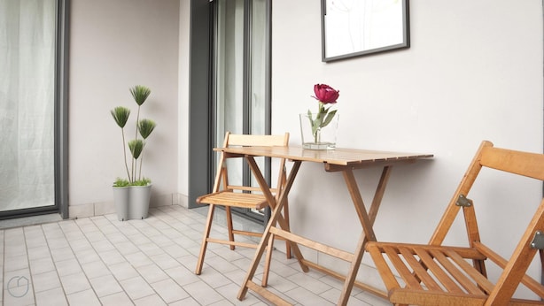 A small, open patio area with a wooden table and chairs, a potted plant, and a framed picture on the wall. - Italianway Comfort - Zanella 10 (Milan)