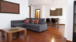 A modern living room with a grey sofa, colorful cushions, a wooden coffee table, and a dining area with a wooden table and chairs. - Italianway Comfort - Zanella 10 (Milan)