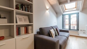 A modern living room with a grey sofa, a bookshelf with books, and a skylight. - Italianway Easy - Savona 108 (Milan)