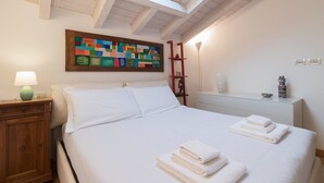 A bedroom with a bed, a nightstand, a lamp, a painting, a shelf with decorative items, and a bedside table. - Italianway Easy - Savona 108 (Milan)