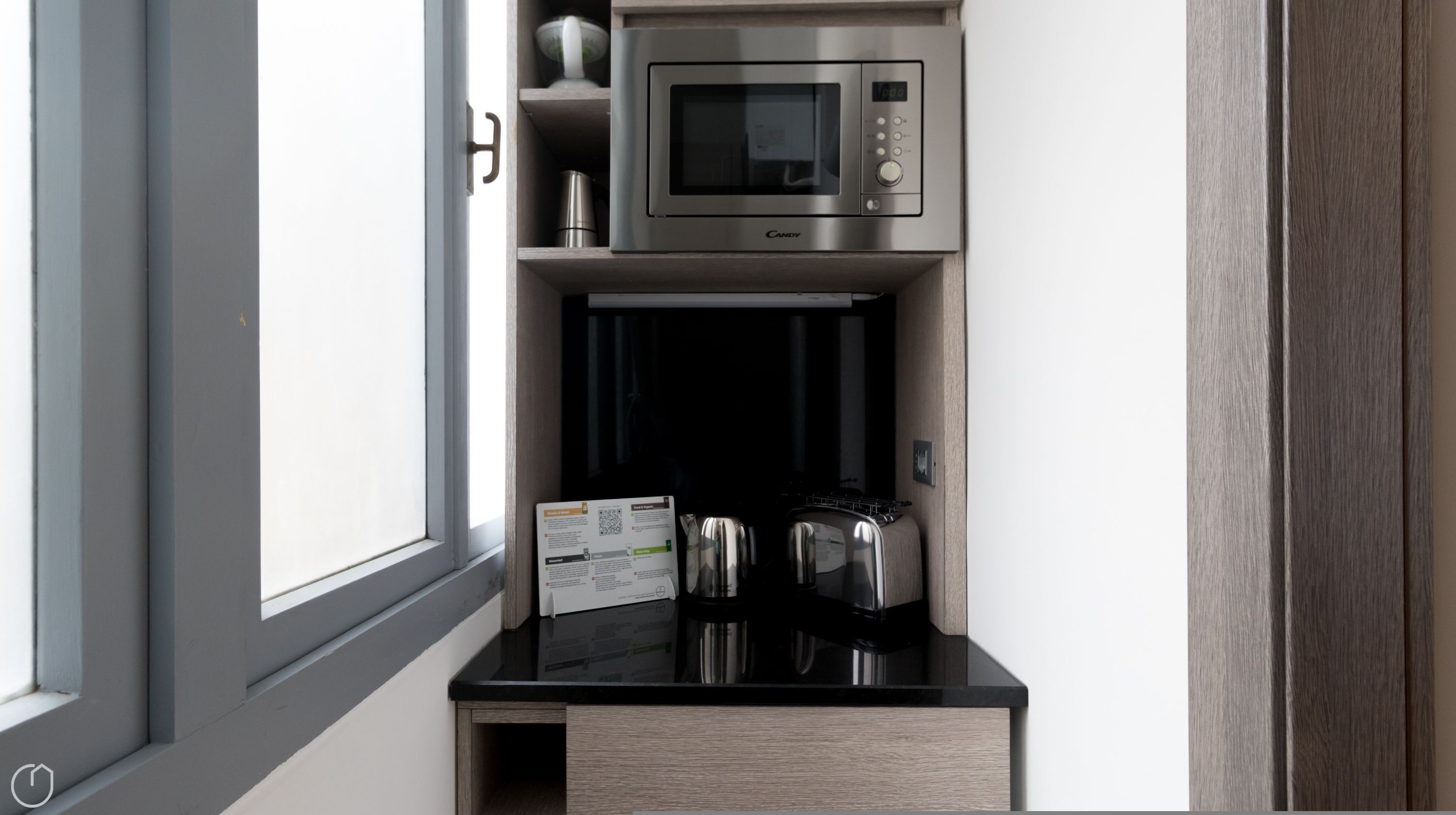 Eine kleine Küchenzeile mit Mikrowelle, Wasserkocher und Kaffeemaschine auf einer schwarzen Arbeitsplatte.