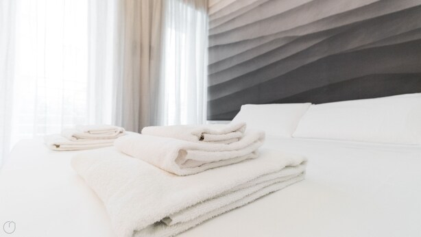 A neatly made bed with folded white towels and a modern, textured wall behind it. - Italianway Easy - Ciro Menotti 18 (Milan)