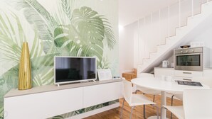 A modern kitchen with a white countertop, a flat-screen TV, a coffee maker, and a wall with a tropical leaf pattern. - Italianway Easy - Ciro Menotti 18 (Milan)