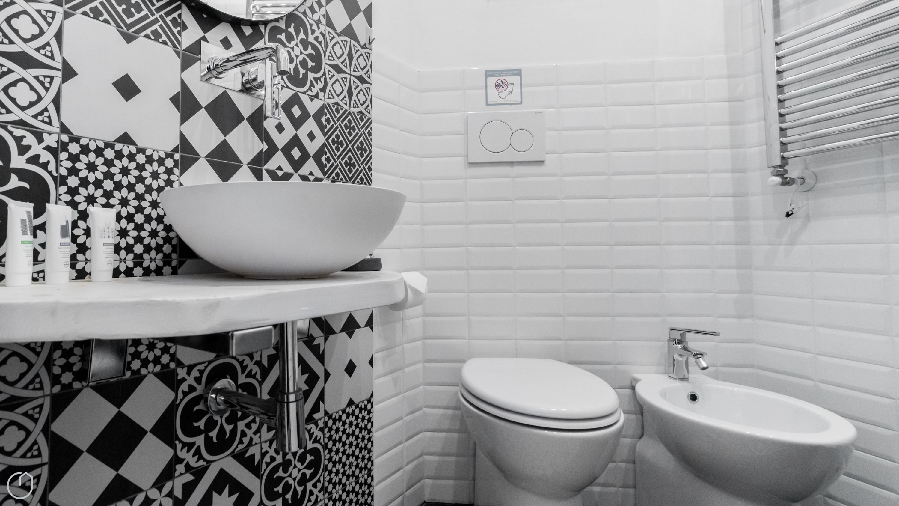 Un baño con lavamanos blanco, lavabo, inodoro y bidé. Las paredes están cubiertas de un patrón blanco y negro.