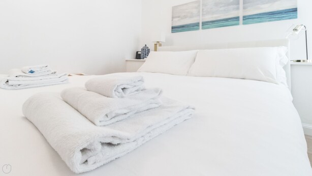 A neatly made bed with white linens and towels, a bedside table with a lamp, and a wall with a painting of a beach scene. - Mi-vige13a3 - Vigevano 13 (Milan)