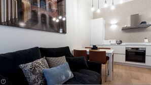 A modern living room with a black sofa, patterned cushions, and a dining area with a white table and brown chairs. A kitchen with white cabinets and stainless steel appliances is visible in the background. - Mi-vige13a3 - Vigevano 13 (Milan)