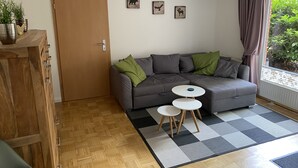 Een moderne woonkamer met een grijze bank, twee kleine witte tafels, een houten kast en een deur.