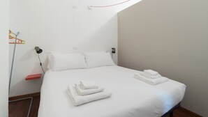 A neatly made bed with white linens and folded towels, a bedside lamp, and a red shelf. - Italianway Easy - Paisiello 4 A (Milan)
