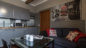 A modern kitchen with grey cabinets, a wooden countertop, and a dining table with a newspaper and coffee mugs. A dark blue sofa with patterned cushions is in the living area, and a large cityscape poster adorns the wall. - Italianway Easy - Paisiello 4 A (Milan)