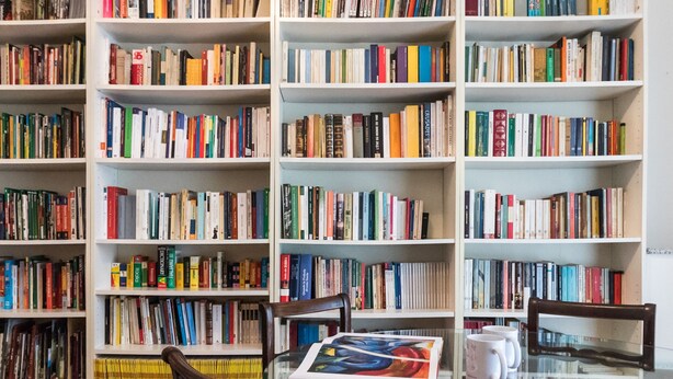 Una biblioteca con estanterías llenas de libros, una mesa de vidrio con sillas y una taza de café.