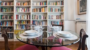 A dining area with a glass table surrounded by chairs, a bookshelf filled with books, and a framed picture on the wall. - Mi-peri5a6 - Pericle 5 (Milan)