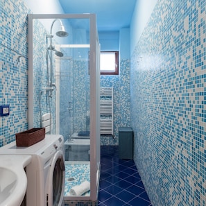 A bathroom with a blue-tiled wall, a glass-enclosed shower, a washing machine, and a toilet. - Mi-peri5a6 - Pericle 5 (Milan)