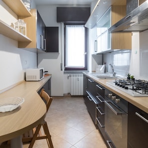 A modern kitchen with a wooden table, a microwave, a gas stove, and cabinets. - Mi-peri5a6 - Pericle 5 (Milan)