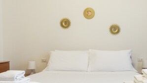 Una cama bien hecha con sábanas blancas y dos adornos dorados en la pared.