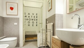 A modern bathroom with a large sink, toilet, and shower area. A sign on the shower door reads "SAVE WATER SHOWER TOGETHER."