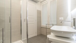 A modern bathroom with a glass shower enclosure, a white sink with a chrome faucet, and a mirror above the sink. - Italianway Easy - Garibaldi 104 A (Milan)