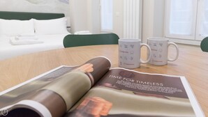 A hotel room with a bed, two white mugs with 'italianway' branding, and a magazine on a table. - Italianway Easy - Garibaldi 104 A (Milan)