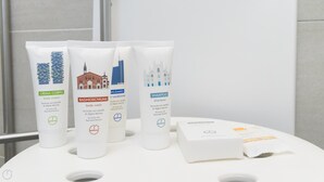 Une salle de bain équipée de quatre produits de toilette : une crème pour le corps, un gel douche, un après-shampoing et un shampoing, chacun présenté dans un tube blanc avec du texte et un logo.