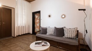 A cozy living room with a wooden floor, a sofa with patterned cushions, a round coffee table with a magazine, and a door with a floral design. - Italianway Easy - Massarani 5 (Milan)