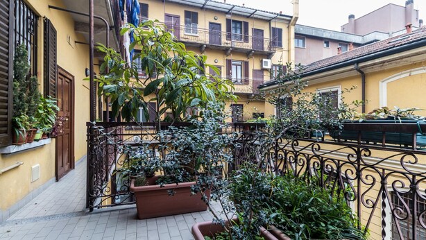 A narrow courtyard with a wrought iron fence, potted plants, and yellow buildings with balconies. - Italianway Easy - Massarani 5 (Milan)