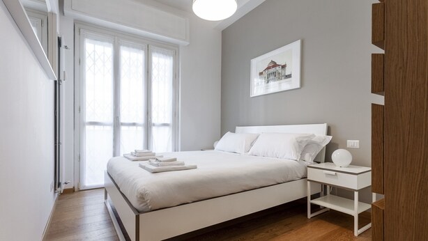 Une chambre à coucher moderne avec un grand lit, une table de chevet et un tableau encadré au mur.