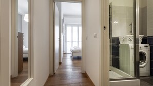 Un couloir d’hôtel avec un lit, un lave-linge et une cabine de douche en verre.