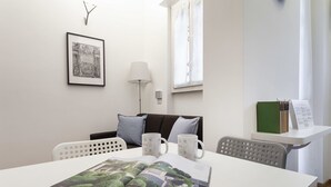 Une chambre moderne avec une table blanche, un tableau encadré au mur, une lampe et une fenêtre avec des rideaux.