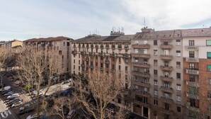 Un edificio residencial de varios pisos con balcones, estacionamiento y árboles sin hojas.