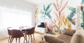 A living room with a dining area, a flat-screen TV, and a large tropical plant wall.