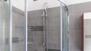 A modern shower area with a glass door, grey tiles, and a metal showerhead. - Italianway Comfort - Antonia Pozzi 5 (Milan)