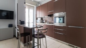 A modern kitchen with a built-in oven, microwave, and a large window. There are two bar stools and a dining table. - Italianway Comfort - Antonia Pozzi 5 (Milan)