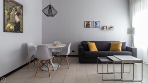 A modern living room with a black sofa, white chairs, a round dining table, and a pendant light. - Italianway Comfort - Antonia Pozzi 5 (Milan)