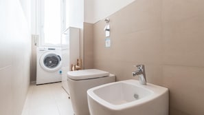 Un baño pequeño con lavadora, dos lavamanos y un inodoro.