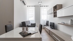 A modern, minimalist office space with a large desk, two chairs, a television, and built-in shelving.