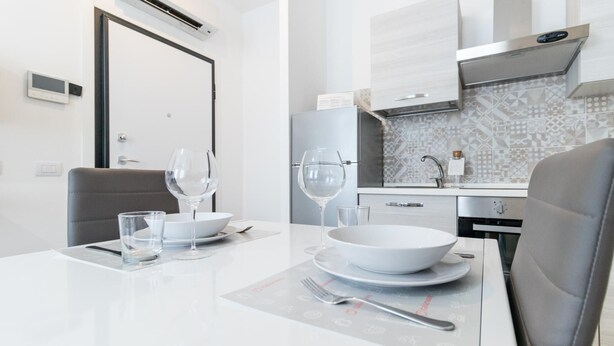 A modern kitchen with white cabinets, a patterned backsplash, and a dining table set with plates, bowls, and wine glasses.