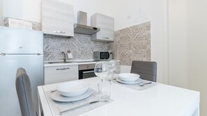 Una cocina moderna con armarios blancos, un microondas y un lavamanos. Hay una mesa de comedor con platos, vasos y cubiertos.