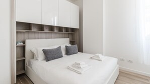 A modern bedroom with a white bed, grey pillows, and a wooden headboard.