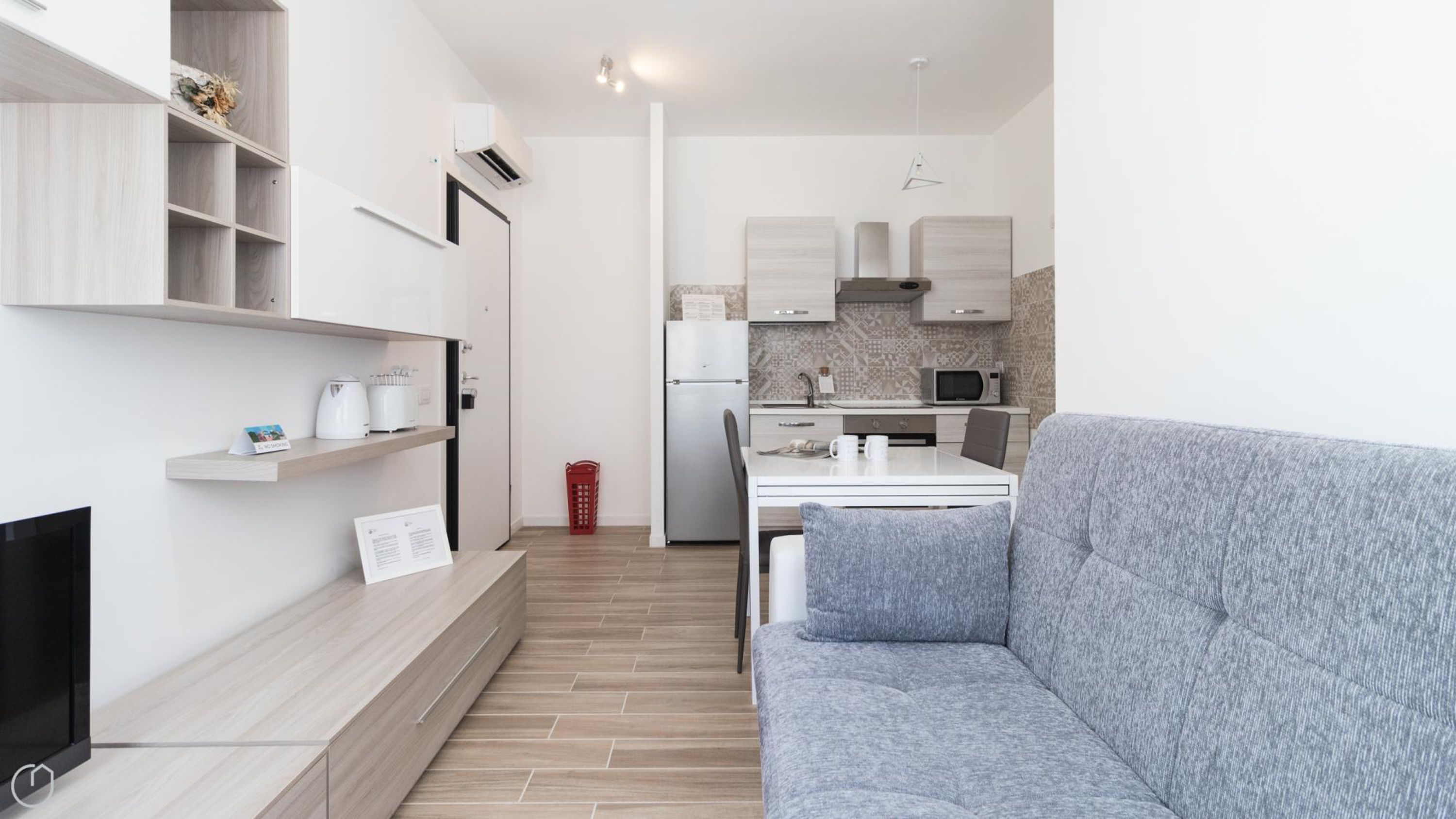 Una sala de estar moderna con un sofá gris, un televisor de pantalla plana y un mueble de entretenimiento de madera.