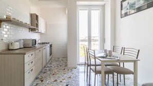 A compact kitchen with white cabinets, a microwave, a toaster, and a stove. There's a dining area with a table and chairs, and a balcony with a view. - Italianway Comfort - Ripa Ticinese 103 (Milan)