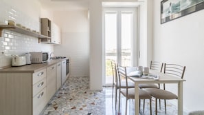 A compact kitchen with white cabinets, a microwave, a toaster, and a stove. There's a dining area with a table and chairs, and a balcony with a view. - Italianway Comfort - Ripa Ticinese 103 (Milan)