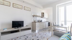 A modern kitchen with white cabinets, a microwave, and a stove. There is a dining table with chairs and a TV on a stand. - Italianway Comfort - Ripa Ticinese 103 (Milan)