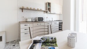A modern kitchen with white cabinetry, a microwave, kettle, and a gas stove. There are shelves above the counter holding jars and a small cabinet. - Italianway Comfort - Ripa Ticinese 103 (Milan)