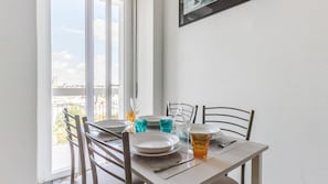 A dining area with a table set for two, chairs, and a view of the city through large windows. - Italianway Comfort - Ripa Ticinese 103 (Milan)