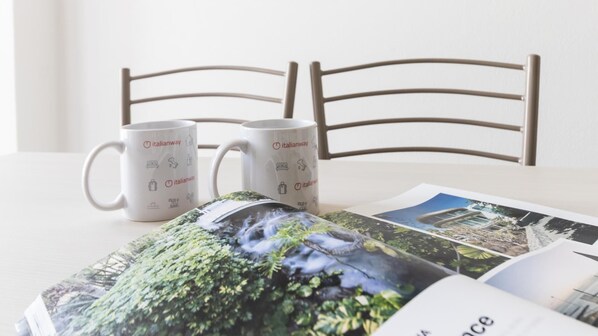 Two white mugs with Italianway logos, a book with a nature image, and a wooden chair. - Italianway Comfort - Ripa Ticinese 103 (Milan)