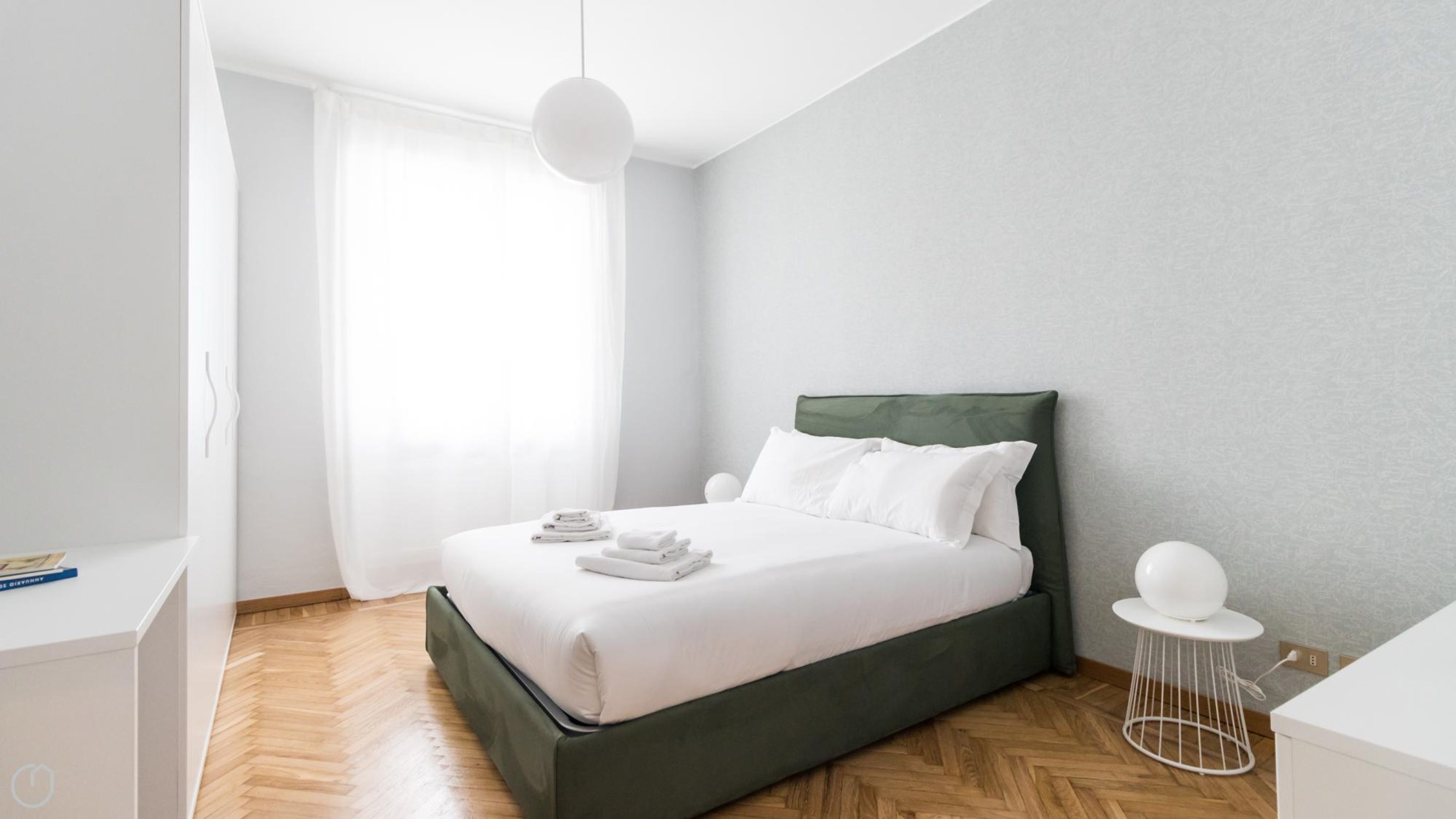 A modern bedroom with a bed, white linens, a green headboard, and a wooden floor.