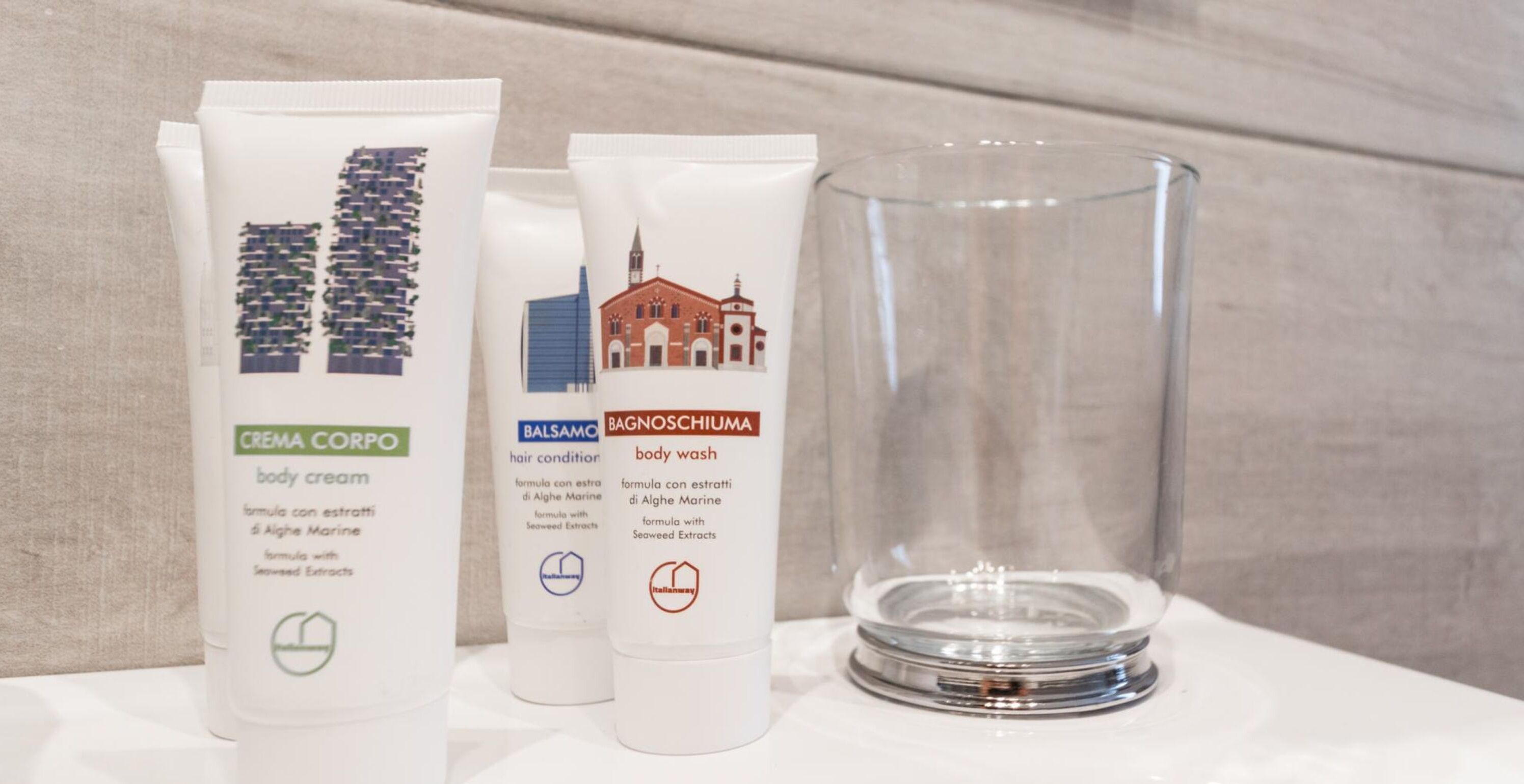 Trois produits de toilette et un verre transparent sur une surface blanche.