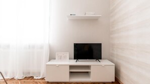 Un meuble de rangement blanc pour appareils multimédias, avec un téléviseur à écran plat, une petite étagère au-dessus et un document posé sur le meuble.