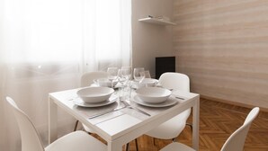 Une table de salle à manger blanche, dressée avec des assiettes, des bols, des verres et des couverts, entourée de chaises blanches dans une pièce lumineuse dont le sol présente un motif en chevrons.