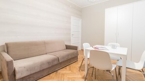 A modern room with a beige sofa, a white dining table, and white chairs. - Italianway Easy - Sacconi 2 A (Milan)